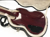 Back side of cherry red electric guitar in black hard case with plush white interior, showing glossy finish and control cavity cover
