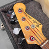 Close-up of Fender Precision Bass headstock with chrome tuning pegs and red wrapped strings in a plush guitar case
