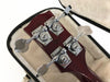 Close-up of bass guitar headstock with chrome Grover tuning pegs and dark wood finish inside plush guitar case