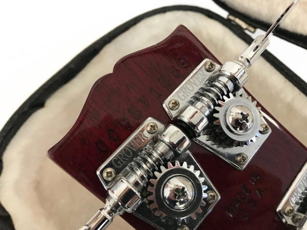 Close-up of vintage Grover tuning pegs on dark red guitar headstock with serial number and case lining background