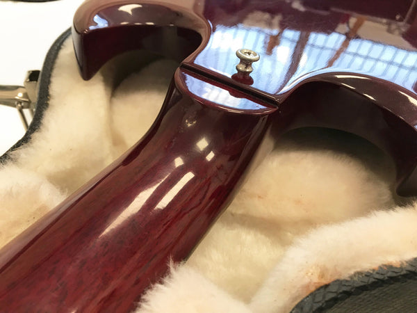 Close-up of glossy cherry red guitar neck and body heel resting on plush cream guitar case lining with metal strap button visible