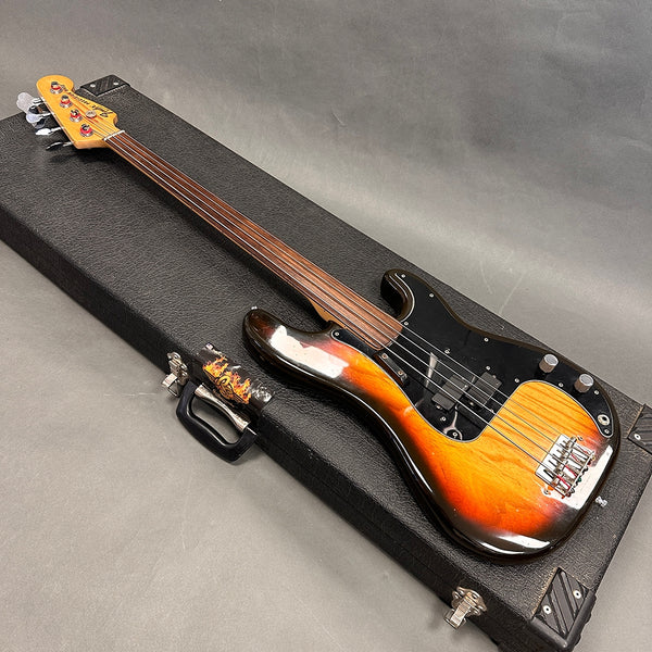 Fender Precision Bass guitar with sunburst finish and fretless rosewood neck resting on black hardshell case