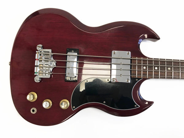 Close-up of cherry red electric bass guitar body with chrome hardware, black pickguard, and three control knobs on a white background