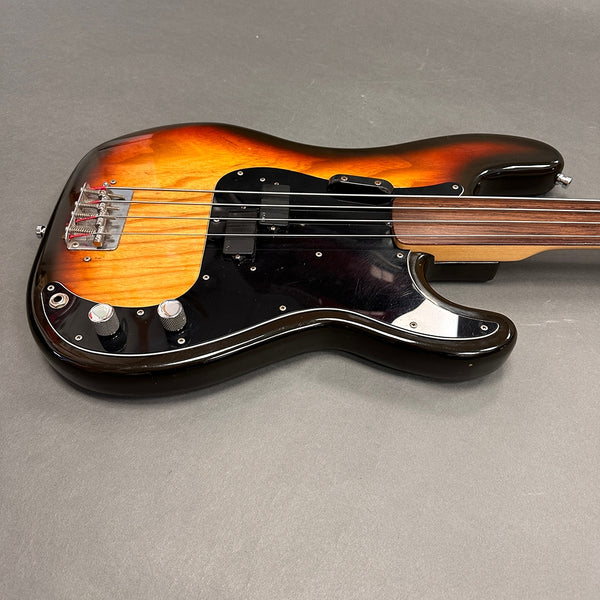 Sunburst electric bass guitar with black pickguard and chrome control knobs on gray background