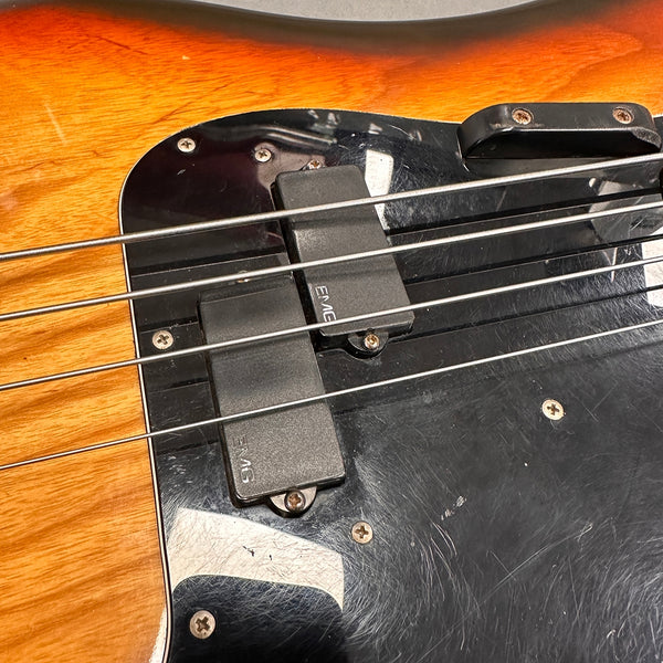 Close-up of electric bass guitar strings and EMG pickups on a natural wood finish body with black pickguard and metal screws