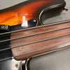 Close-up of sunburst electric bass guitar with smooth wooden fretless fingerboard and four metal strings on gray surface
