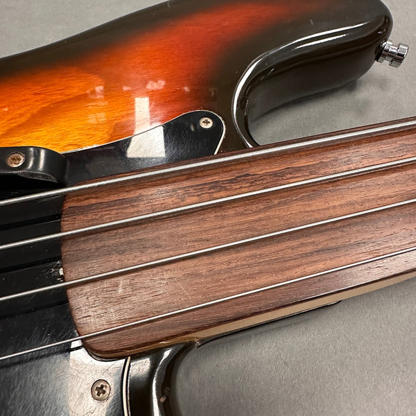Close-up of sunburst electric bass guitar with smooth wooden fretless fingerboard and four metal strings on gray surface