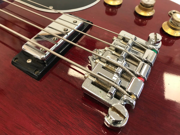 Close-up of chrome bridge and pickups on red electric bass guitar with tone control knobs