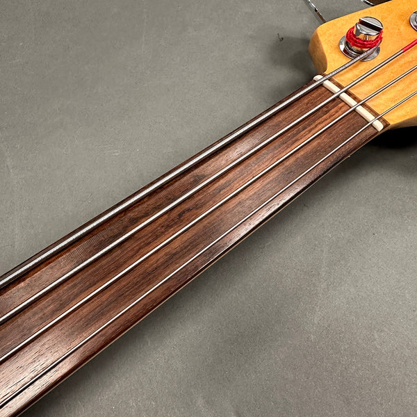 Close-up of fretless bass guitar neck with rosewood fingerboard and four strings on gray background