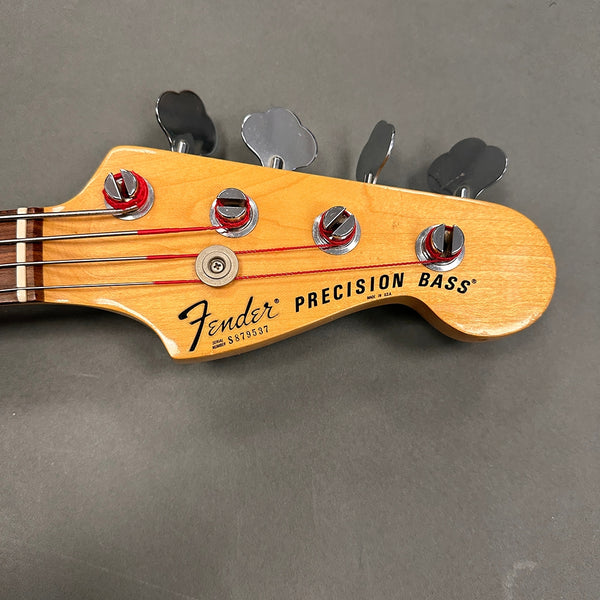 Close-up of Fender Precision Bass headstock with tuning pegs and strings on gray background