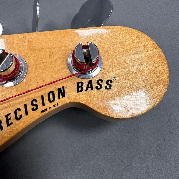 Close-up of natural wood Precision Bass guitar headstock with chrome tuning pegs and red string winding, made in USA text visible