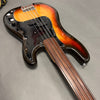 Fretless electric bass guitar with sunburst finish, black pickguard, and wooden fingerboard, displayed on gray surface.