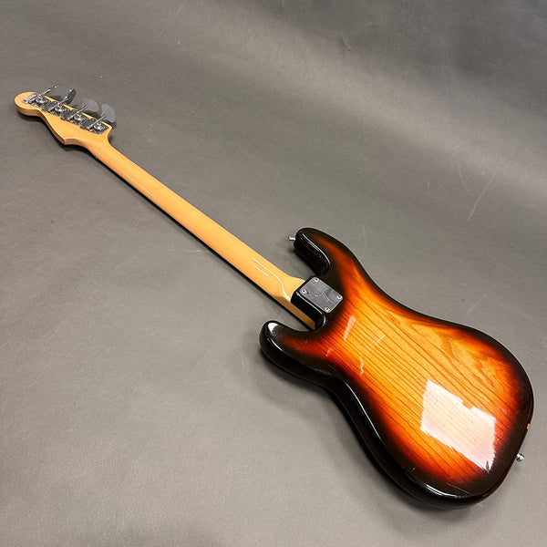 Back view of sunburst electric bass guitar with maple neck and chrome tuning pegs on gray background