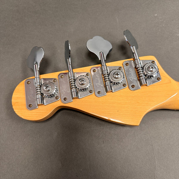 Close-up view of Fender bass guitar tuning pegs on natural wood headstock with chrome hardware