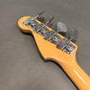 Close-up of natural wood finish bass guitar headstock with four chrome Fender tuning pegs on gray background.