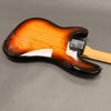 Electric guitar body back view with sunburst finish and maple neck, showing neck plate and strap button on gray background