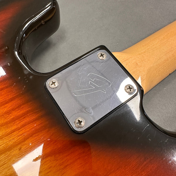 Close-up of neck plate on sunburst electric guitar with four screws and engraved logo on metal plate