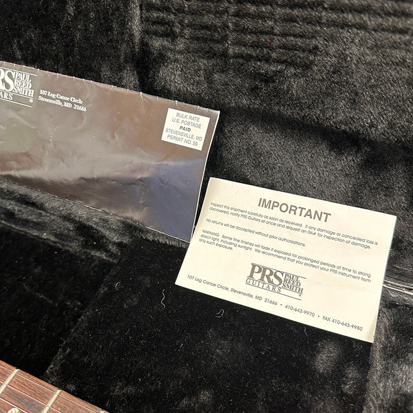 Paul Reed Smith PRS Guitars warranty and important care information card inside guitar case with plush black interior lining, partial view of guitar neck.
