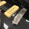 Close-up of black electric guitar showing cream-colored single-coil pickup, chrome bridge, and black tone control knob