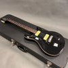 Black electric guitar with dual cream-colored pickups, black knobs, and a rosewood fretboard on black hard case.