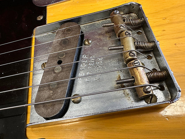 Close-up of vintage Fender Telecaster electric guitar bridge and single-coil pickup with six metal strings on natural wood body