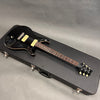 Black electric guitar with cream pickups and knobs on black hard case, six-string with rosewood fretboard and dot inlays, guitar headstock with tuning pegs and logo, studio background.