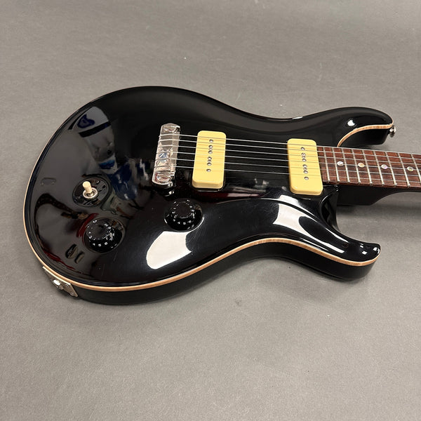 Black electric guitar with cream-colored pickups, two black control knobs, and toggle switch on a gray background