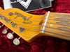Close-up of Fender electric guitar headstock with tuning pegs and strings on red velvet background