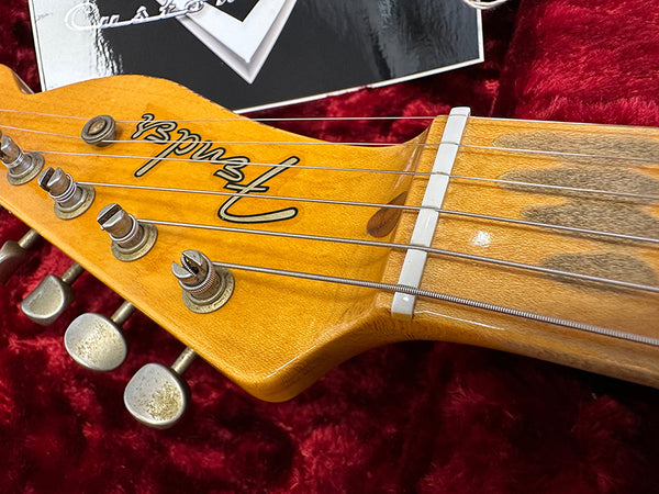 Close-up of Fender electric guitar headstock with tuning pegs and strings on red velvet background