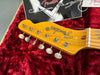 Close-up of vintage Fender guitar headstock with tuning pegs on red velvet case interior and Fender Custom Shop tags