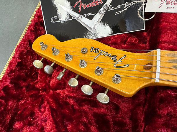 Close-up of vintage Fender guitar headstock with tuning pegs on red velvet case interior and Fender Custom Shop tags