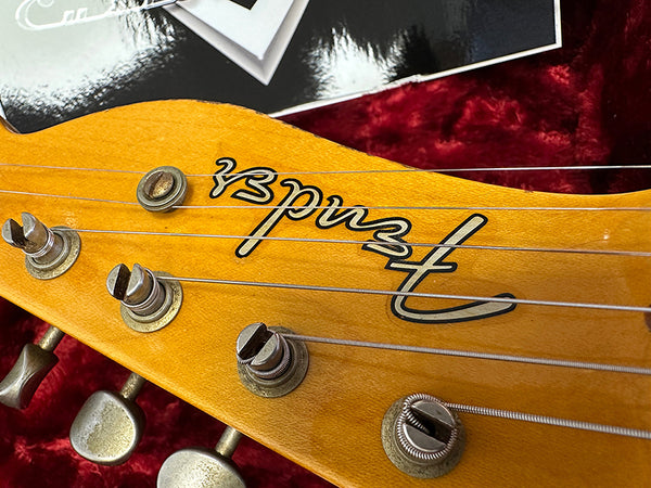 Close-up of Fender guitar headstock with tuning pegs and strings on a red velvet background