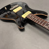 Black electric guitar with cream P90 pickups and rosewood fretboard on gray surface