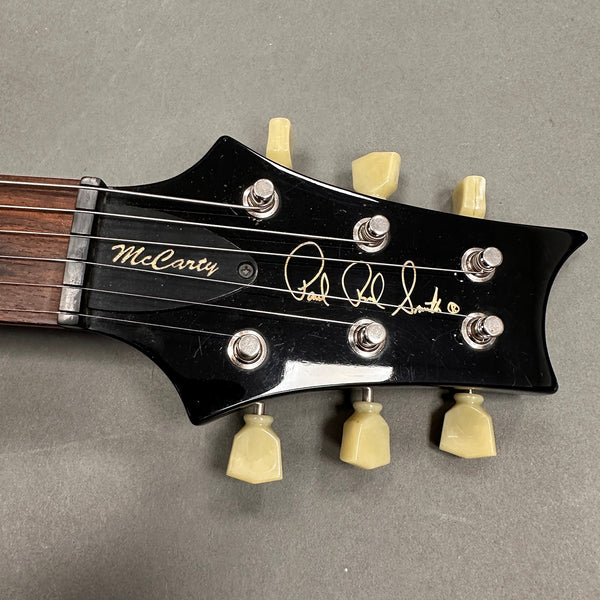 Close-up of black Paul Reed Smith McCarty guitar headstock with cream tuning pegs and visible strings on gray background