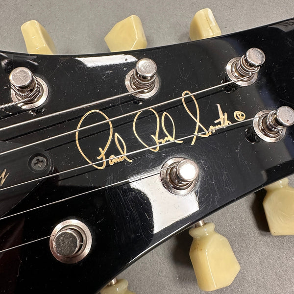 Close-up of black guitar headstock with Paul Reed Smith signature and cream tuning pegs