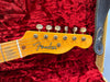 Close-up of Fender electric guitar headstock with vintage tuning pegs and logo on maple neck, resting on red plush guitar case lining with Fender strap visible