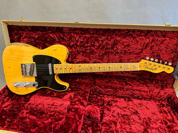 Vintage Fender Telecaster electric guitar with worn butterscotch finish and black pickguard resting in red velvet-lined guitar case