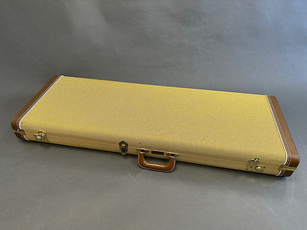 Closed tan tweed guitar hard case with brown leather handle and corner reinforcements on gray background