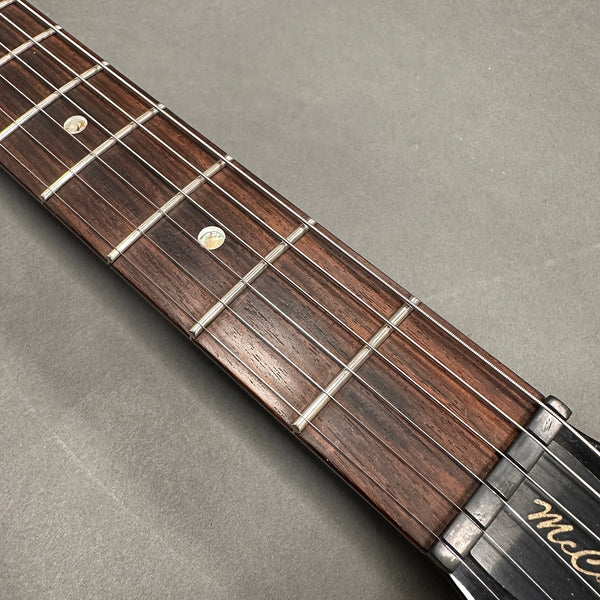 Close-up of guitar fretboard with metal frets, pearl inlay dots, and steel strings on a wooden neck against a gray background