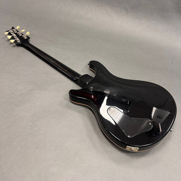 Black electric guitar backside showing neck, body, and control cavity cover on gray background