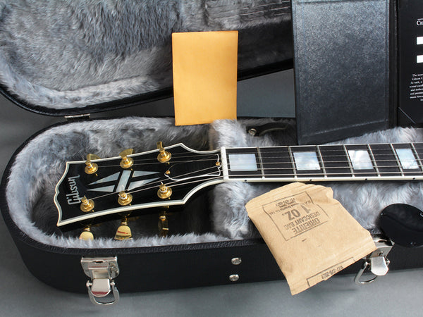 Gibson electric guitar headstock with gold tuning pegs in gray plush-lined hard case with desiccant packets and paperwork