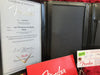 Fender Certificate of Authenticity for 1957 Stratocaster Jrny Relic with serial number R91935 and Fender Custom Shop logo in black leather folder with Fender manual and tags on red background