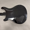 Back side of black electric guitar with curved body and rear control cavity cover on gray background