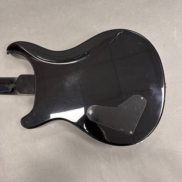 Back side of black electric guitar with curved body and rear control cavity cover on gray background