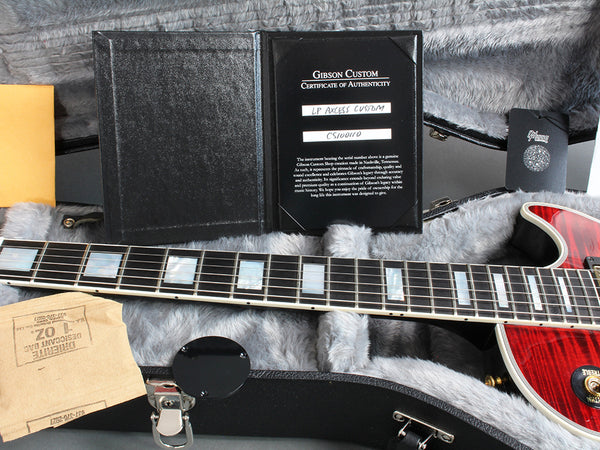 Gibson Custom LP Axcess Custom guitar certificate of authenticity displayed inside guitar case with plush gray interior and guitar neck showing mother of pearl inlays and red finish.