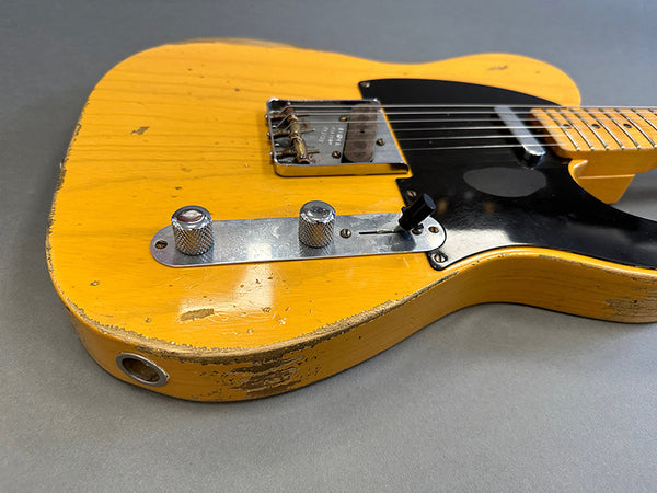 Close-up of vintage yellow electric guitar body with black pickguard and chrome control knobs showing worn and chipped paint details