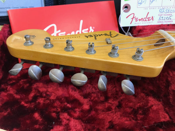 Close-up of vintage Fender Stratocaster maple guitar headstock with six tuning pegs and strings, resting on red plush guitar case lining with Fender logo tag in background.