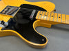 Close-up of vintage yellow electric guitar with black pickguard and maple fretboard on gray background