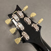 Close-up of black guitar headstock with six vintage-style tuning pegs and serial number 159298 visible on back of headstock.