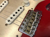 Close-up of red electric guitar bridge and white single-coil pickups with volume knob, showcasing Fender vintage-style saddles and metal hardware.